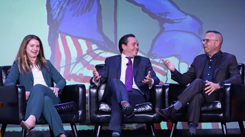 Three panelists in conversation on a lit stage